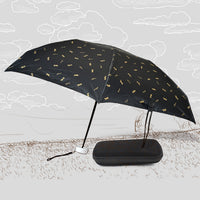 A black DrizzlePro umbrella with small gold musical note patterns is open next to its black zippered case on a sketched