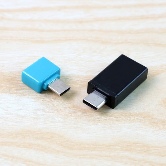 Blue Micro USB and black USB-C OTG adapters on a light wooden surface.