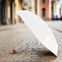 A white umbrella with a red handle stands open on a cobblestone street, ready for use.